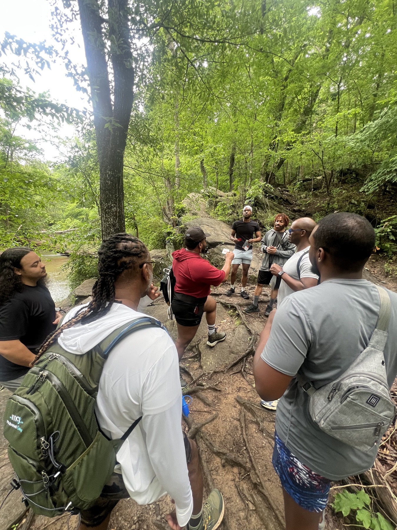 A group of Black hikers follow a rugged path between rock walls and leafy trees.