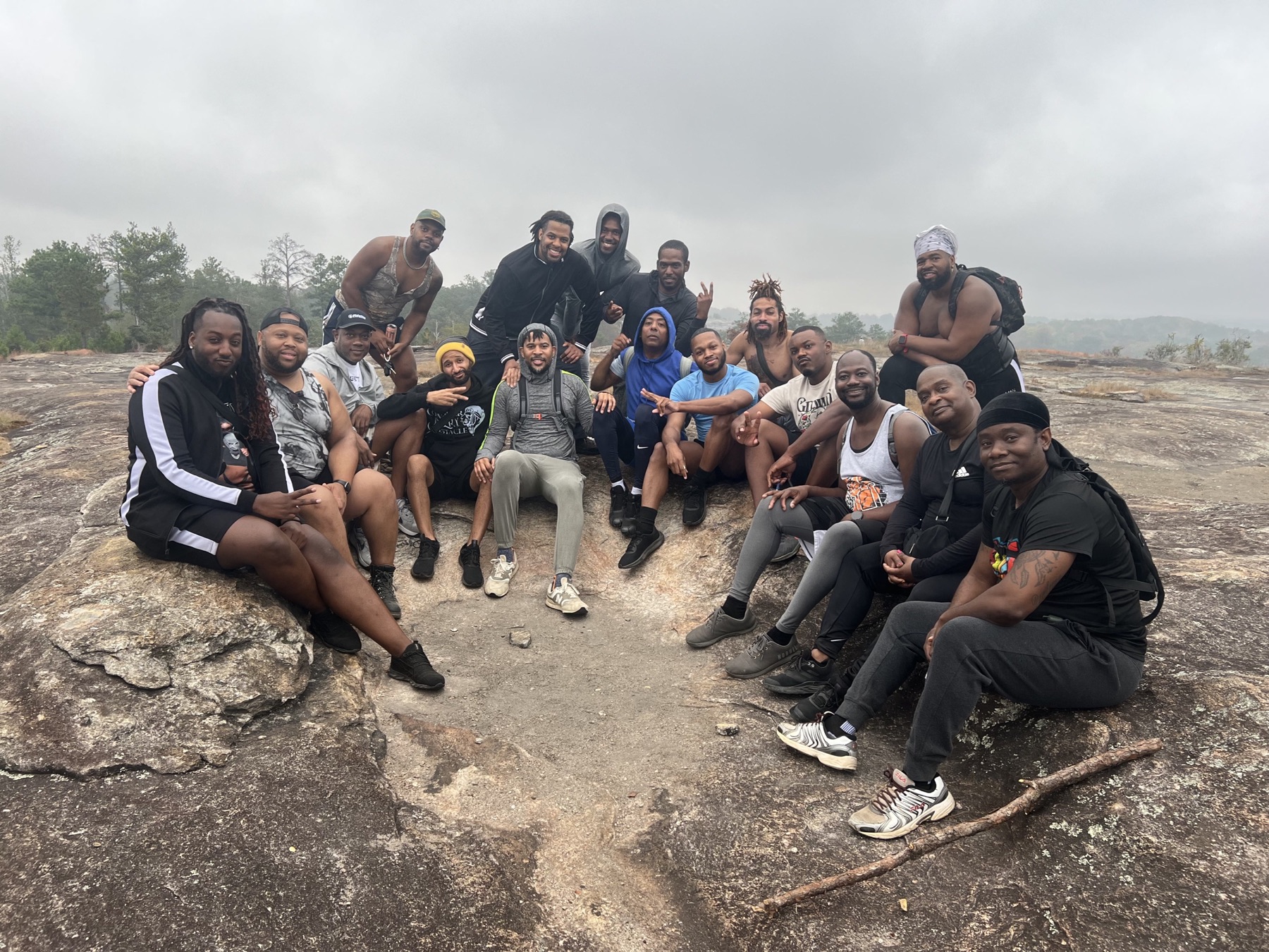 Black men sit and stand together on a granite outcrop under an overcast sky.